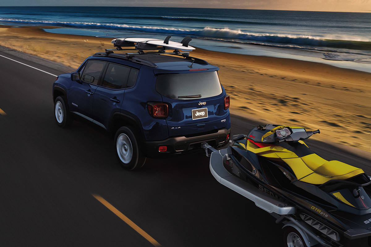 Un Jeep Renegade remorquant une motomarine sur une route longeant une plage
