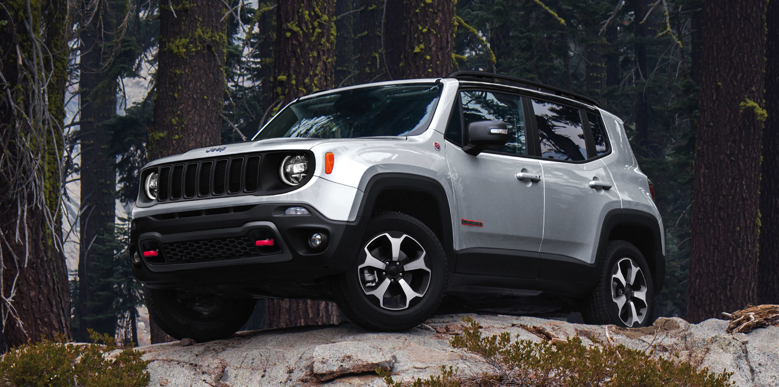 Jeep Renegade argent garé sur une colline rocheuse à la lisière d’une forêt.