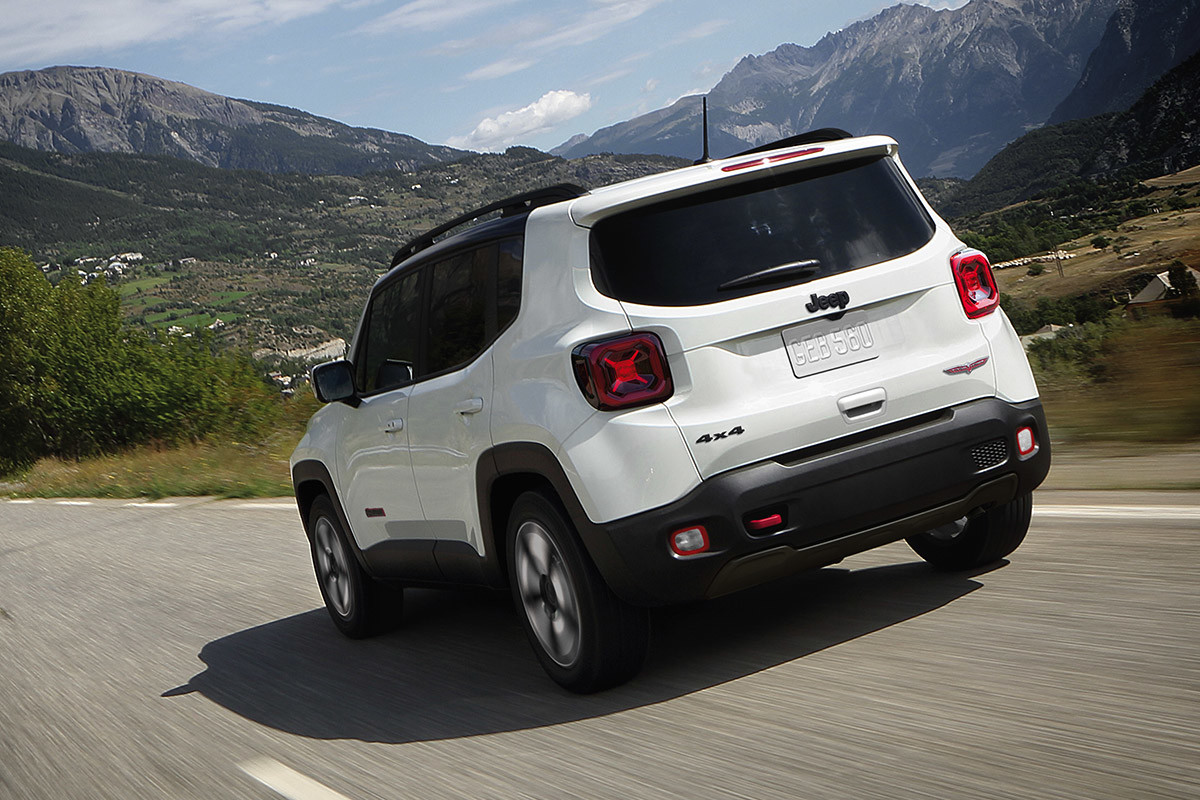 White Jeep Renegade driving on a road with trees and mountains ahead.