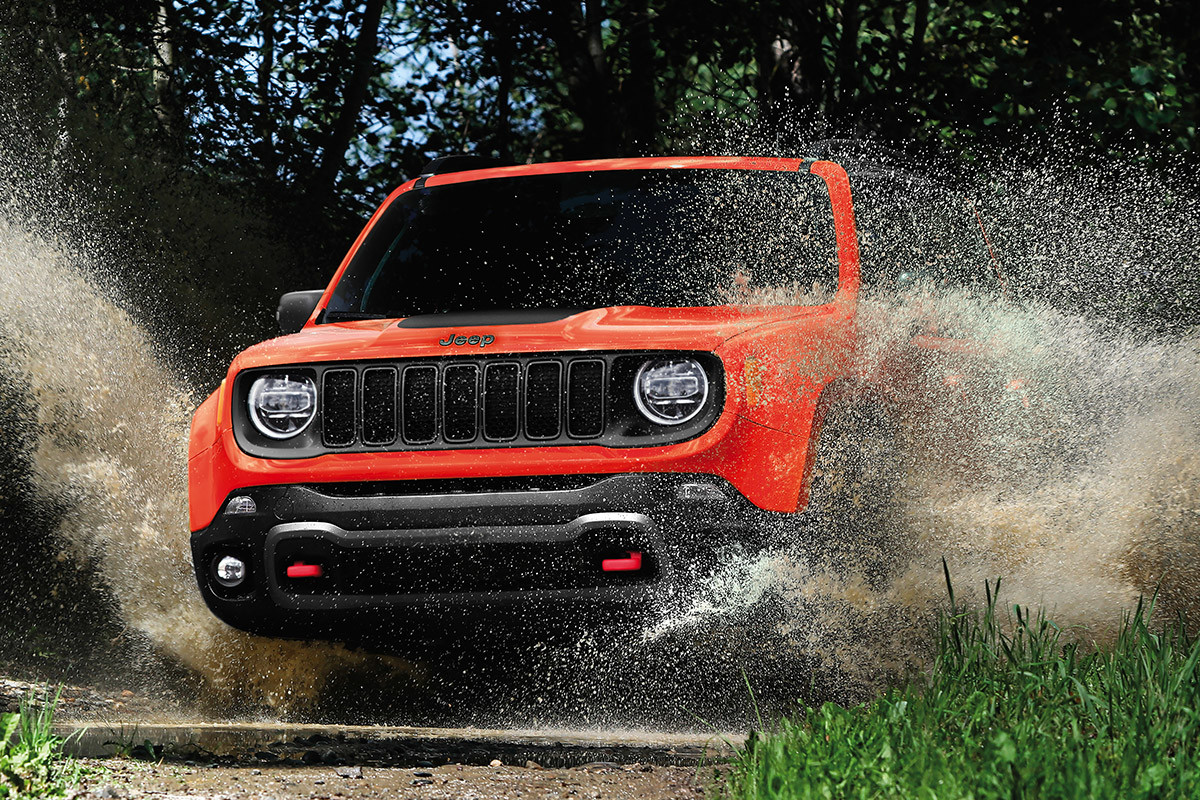 Red Jeep Renegade fording through water on an off-road trail.