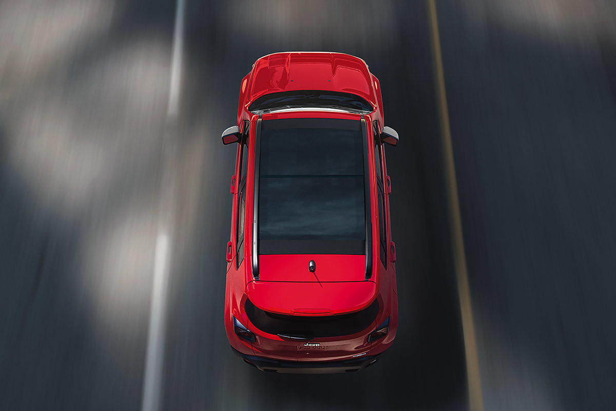 Vue aérienne d’un Jeep Renegade rouge roulant sur une route.