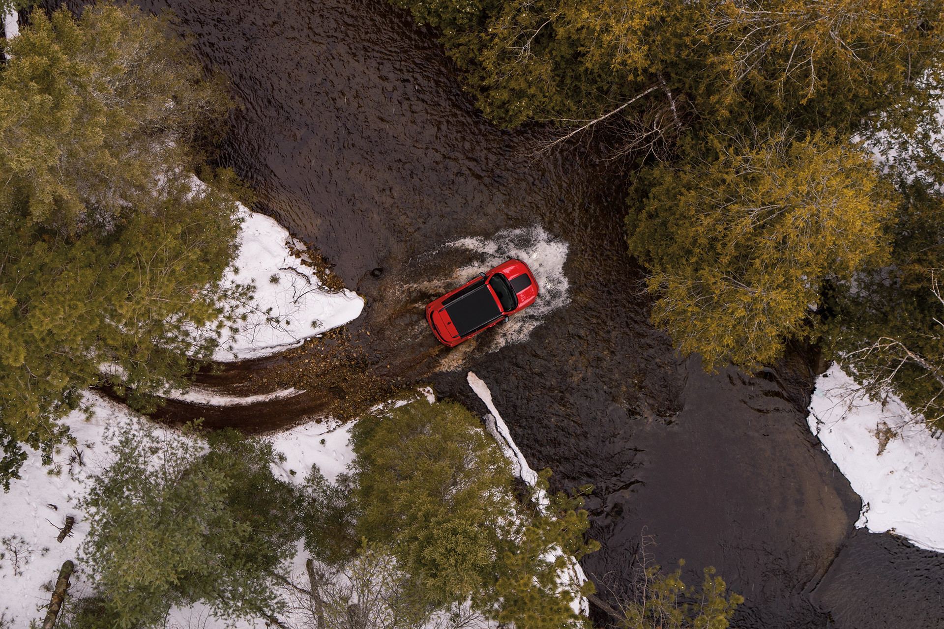 A birds eye view of a red 2022 Jeep Renegade driving through a river.