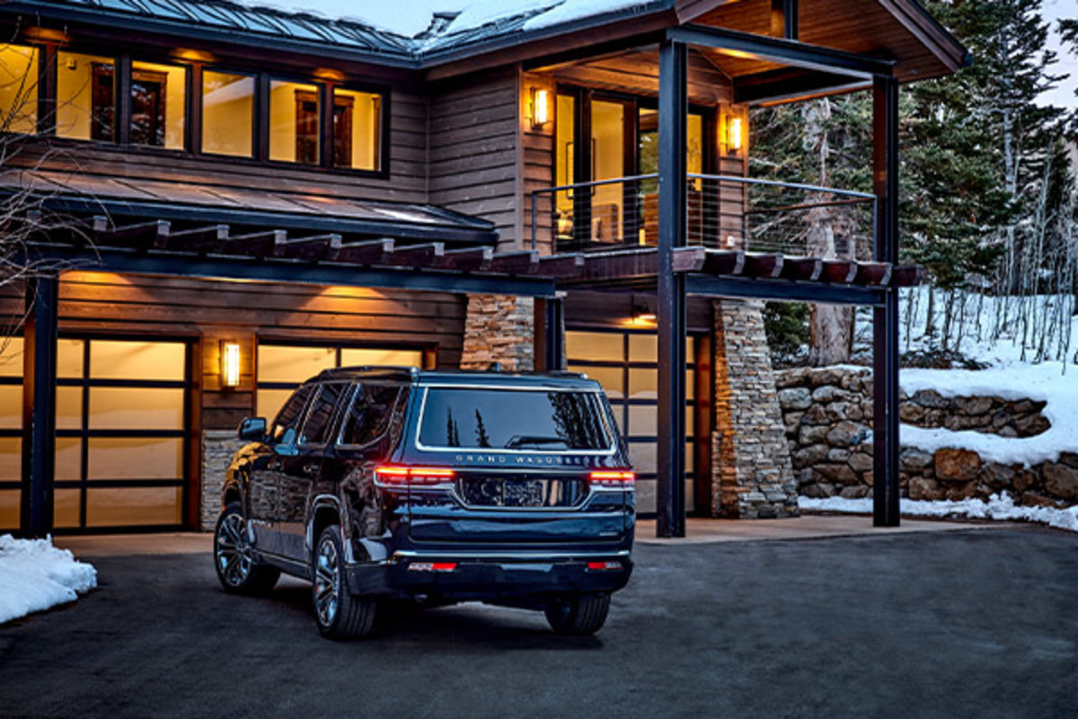Back view of a 2022 black Grand Wagoneer, parked in front of a house in the mountains