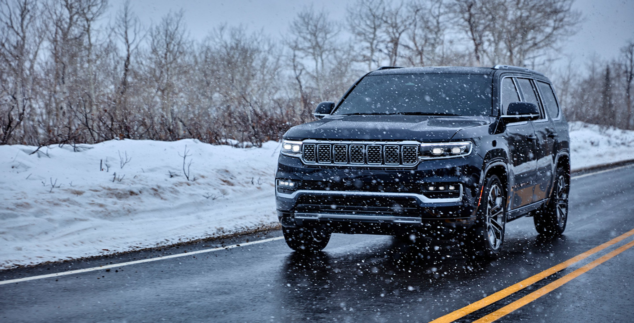 Vue avant d’un Grand Wagoneer 2022 noir roulant sur une route pendant une tempête de neige