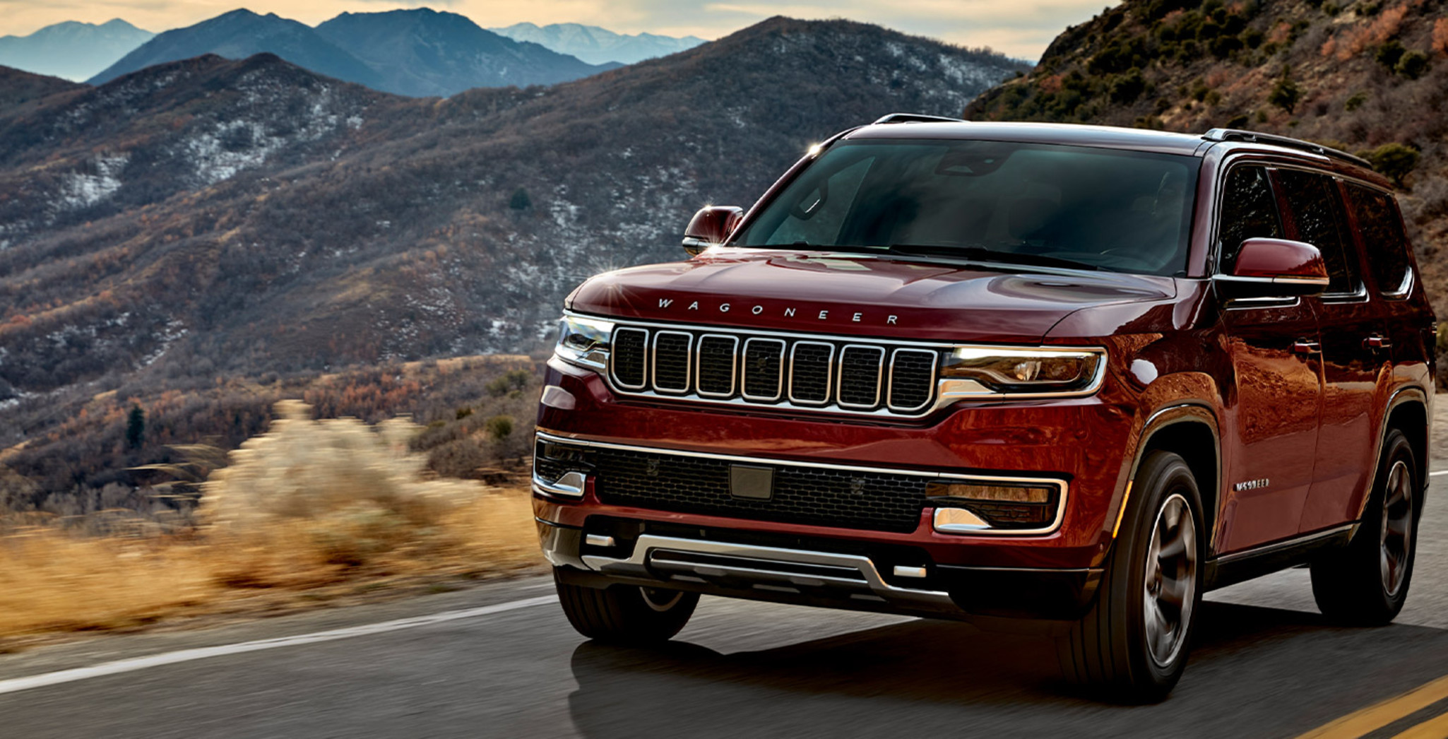 Vue de devant du Grand Wagoneer 2022 rouge roulant sur une route asphaltée avec des montagnes en arrière-plan
