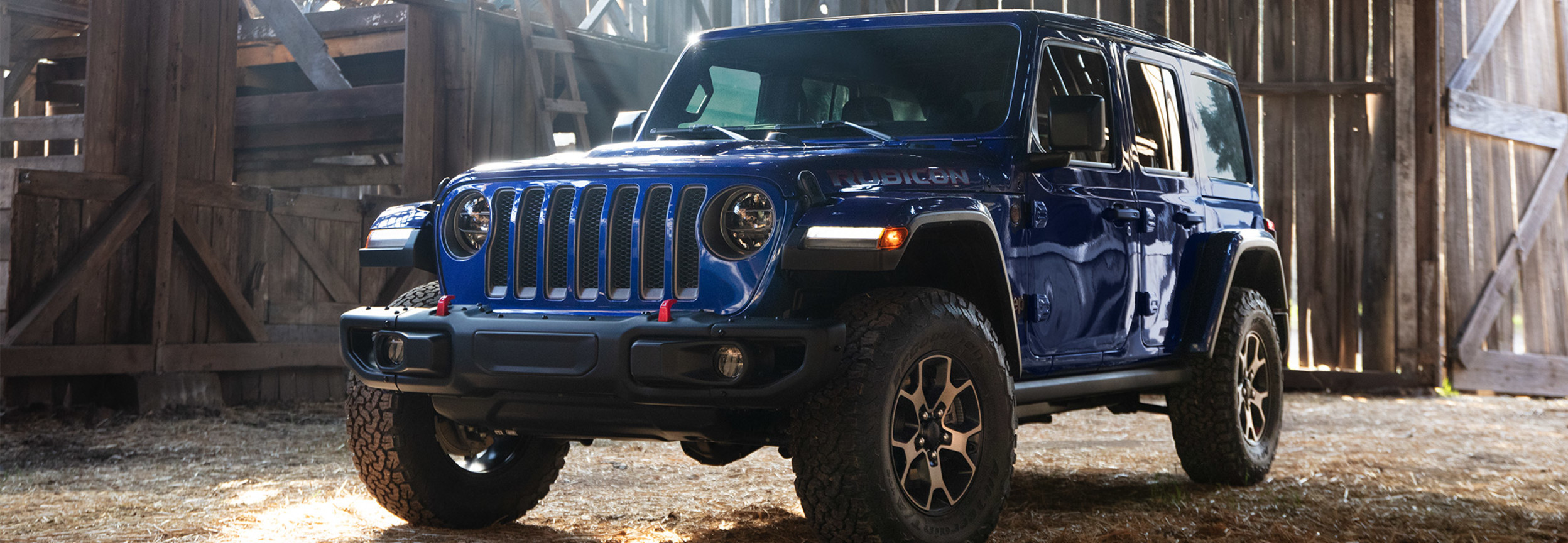 Side view of a blue Jeep Wrangler parked in a horse shed