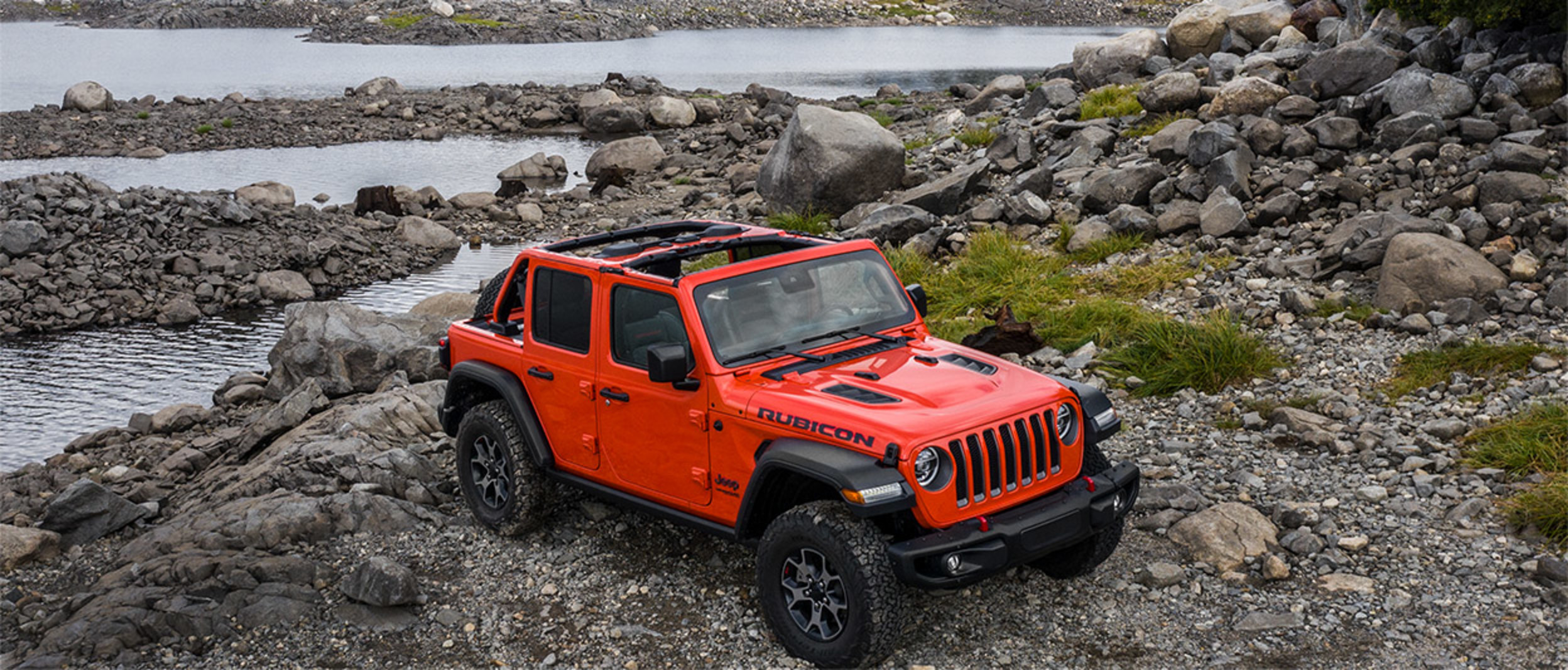 Un Jeep Wrangler 2020 rouge stationné près d’un lac avec des montagnes en arrière-plan