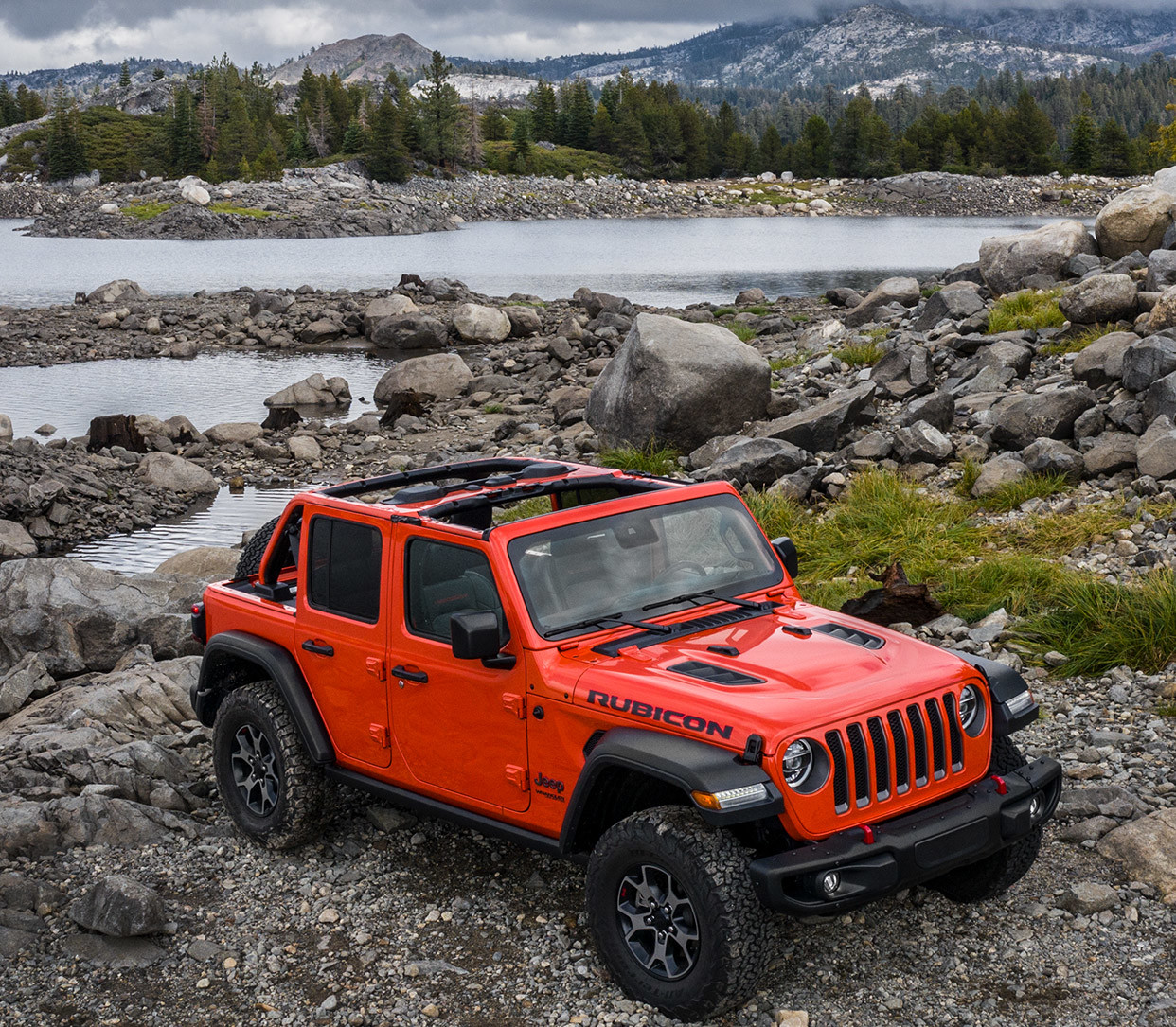 Un Jeep Wrangler 2020 rouge stationné près d’un lac avec des montagnes en arrière-plan
