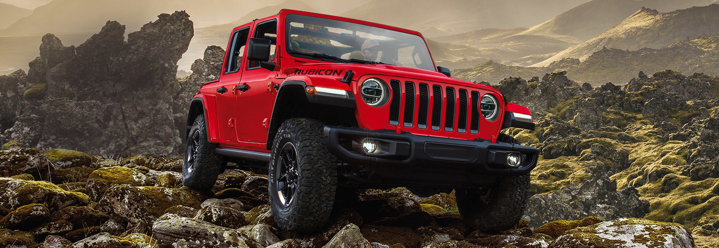 Jeep Wrangler 2021 rouge roulant sur un terrain rocheux avec des montagnes en arrière-plan.