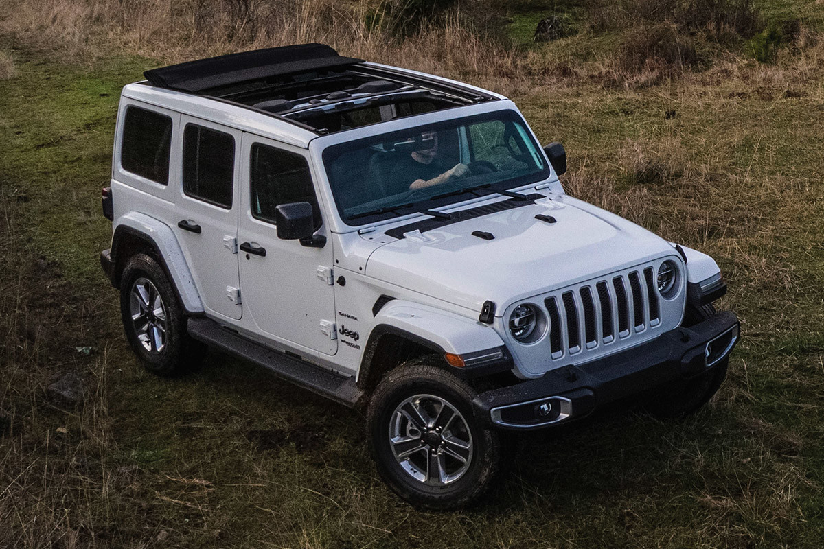 Jeep Wrangler 2021 blanc, garé au sommet d’une colline verdoyante avec des arbres, des collines et des montagnes en arrière-plan
