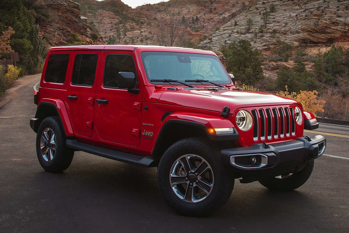 Jeep Wrangler 2021 rouge garé dans la nature, devant des montagnes.