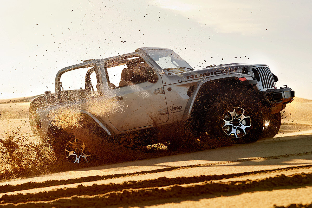 Un Jeep Sahara Rubicon argent roulant à travers une dune, sans son toit.