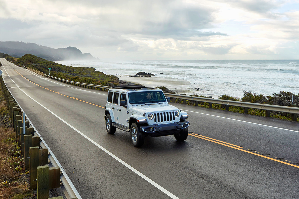 2022 Wrangler Unlimited Sahara in Bright White, driving down paved coastal road.