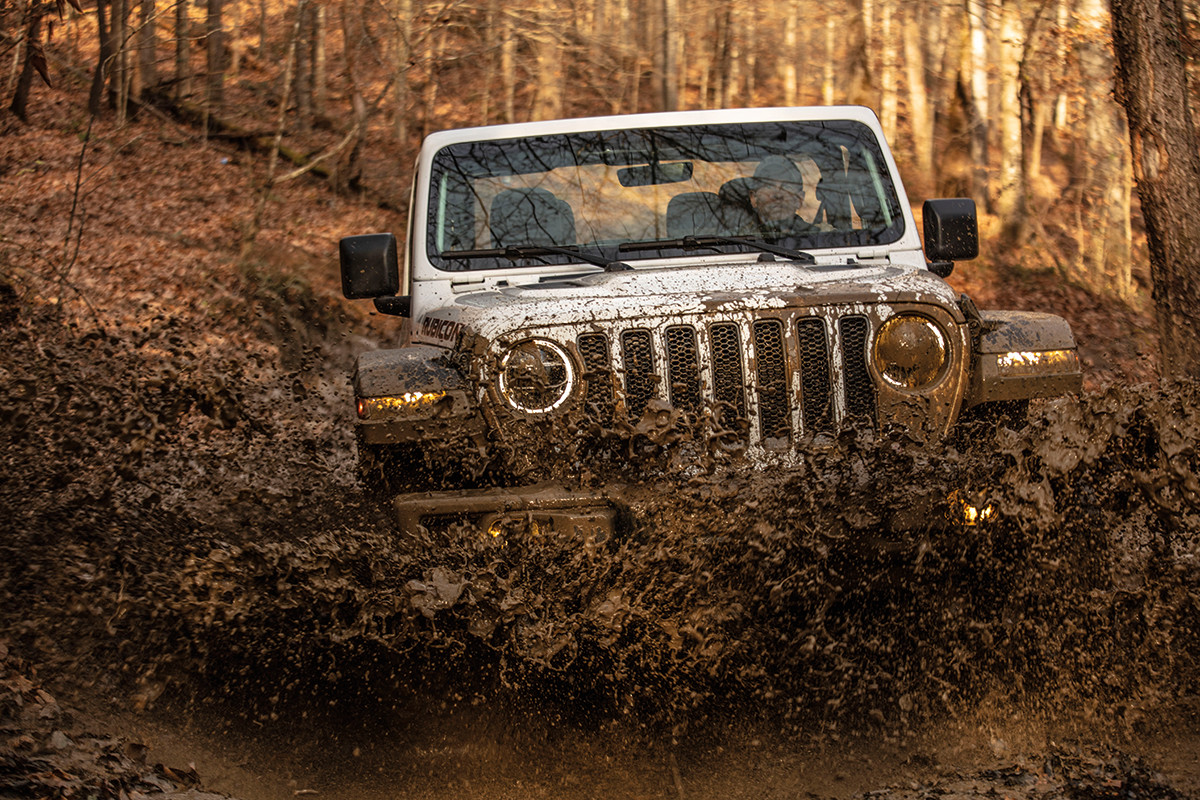 Jeep Wrangler blanc roulant dans la boue dans un décor de forêt.
