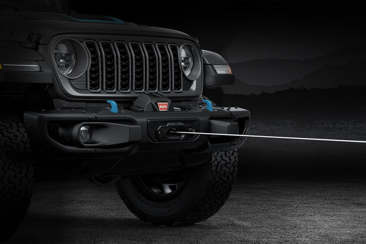 A left profile view of a black 2024 Jeep Wrangler shown using factory-installed winch.