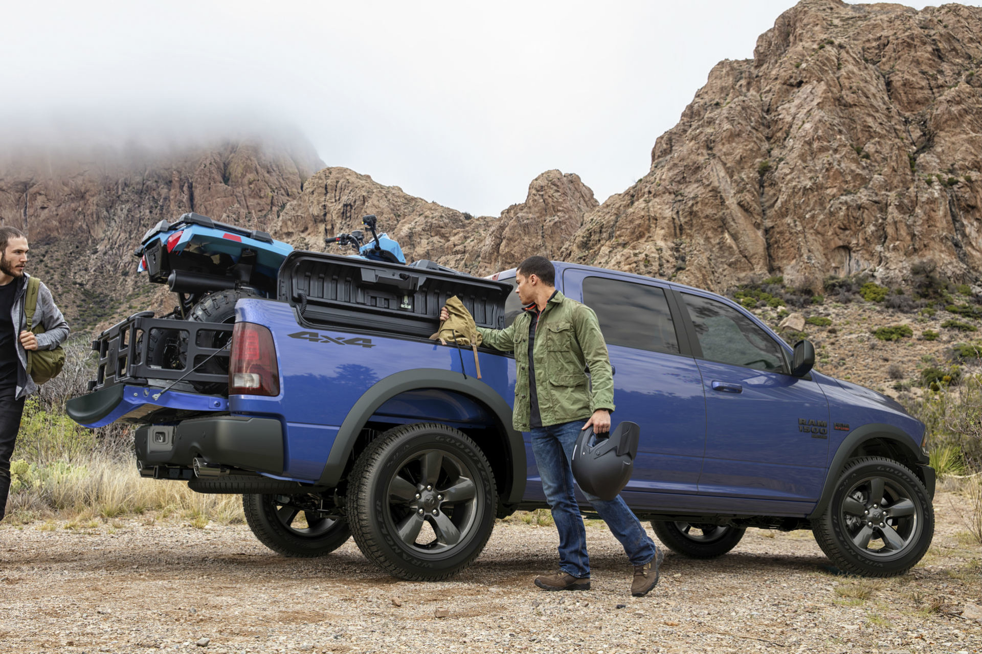 Deux hommes chargent un véhicule tout-terrain dans le Ram 1500 Classic 2019, illustré en bleu, dans les montagnes Rocheuses
