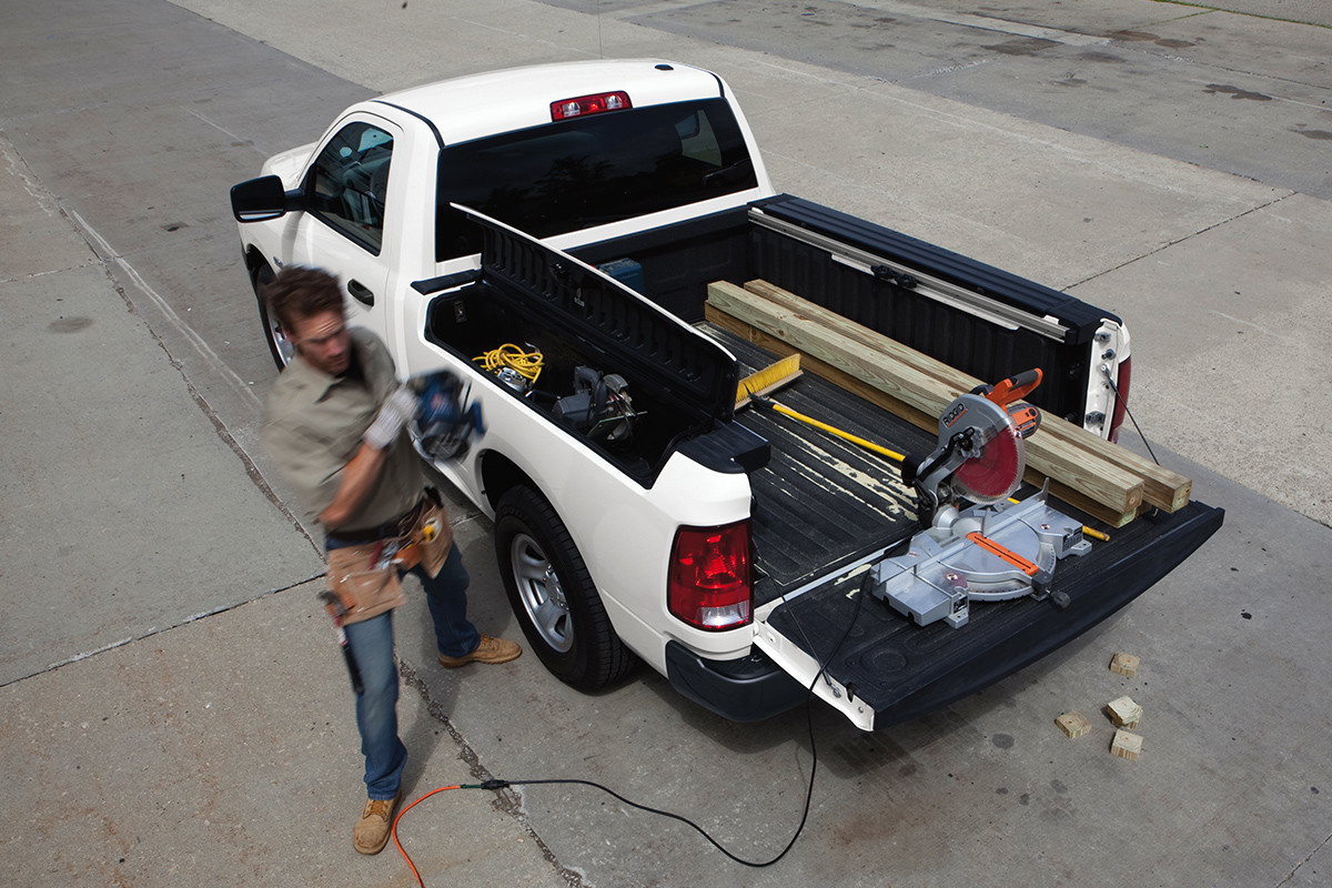 Top-down view of the white 2020 Ram 1500 parked with the rear cargo door opened while worker walks beside it