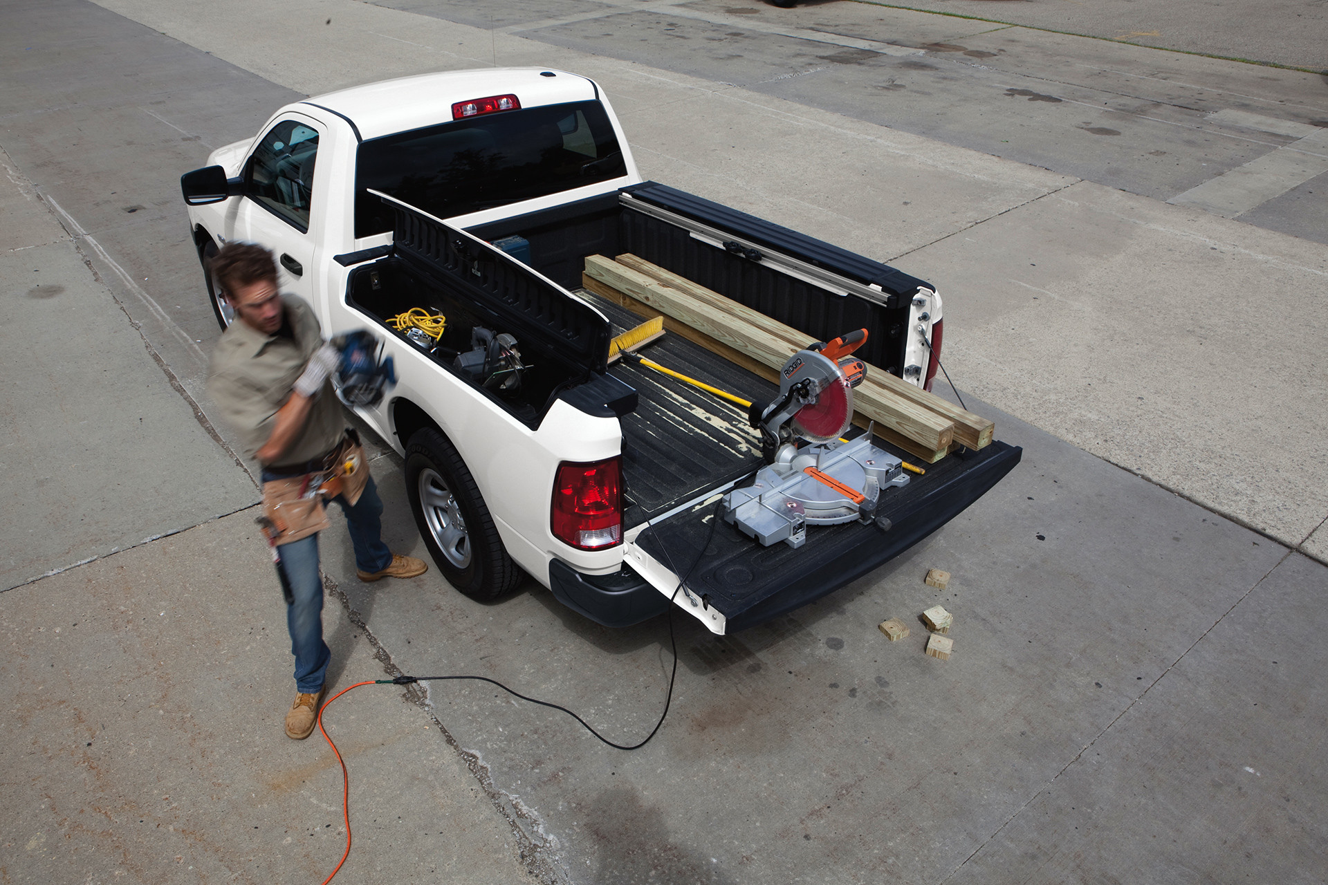 Top-down view of the white 2020 Ram 1500 parked with the rear cargo door opened while worker walks beside it