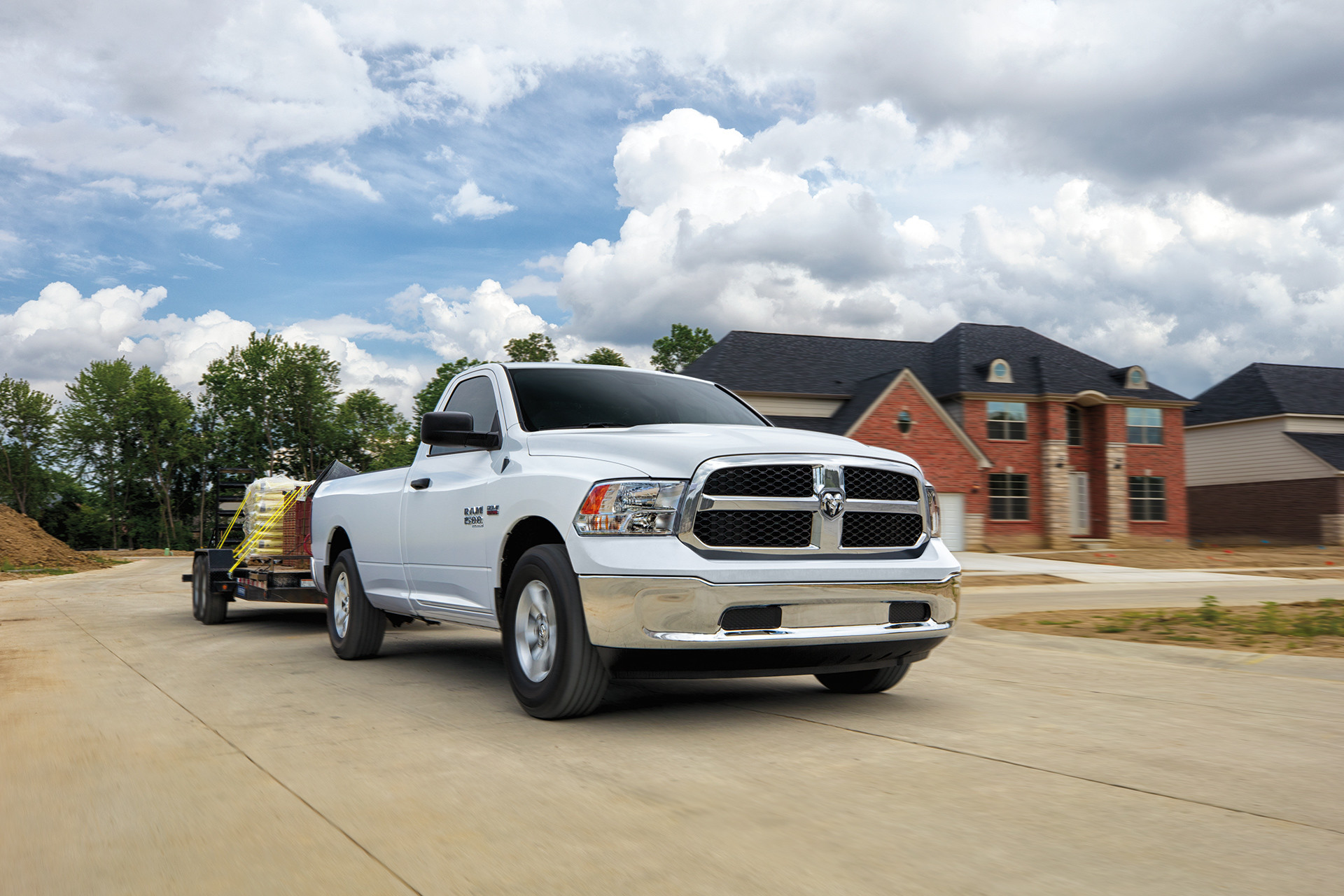 Front view of the white Ram 1500 Classic, towing a utility trailer down a suburban street