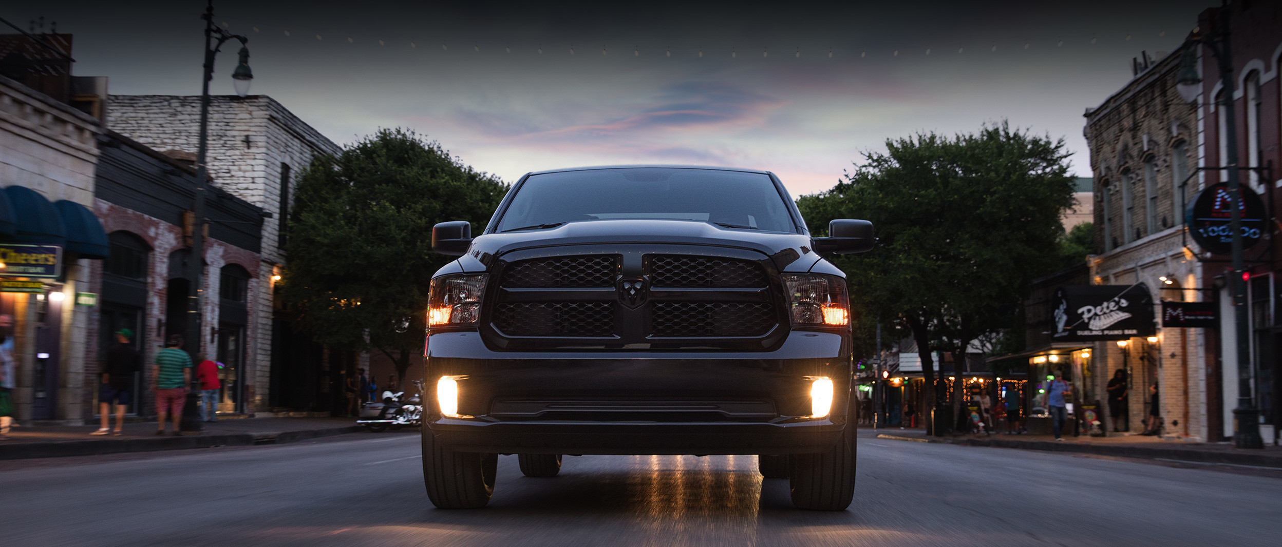 Front view of the black 2020 Ram 1500 Classic driving on a town street at sunset.