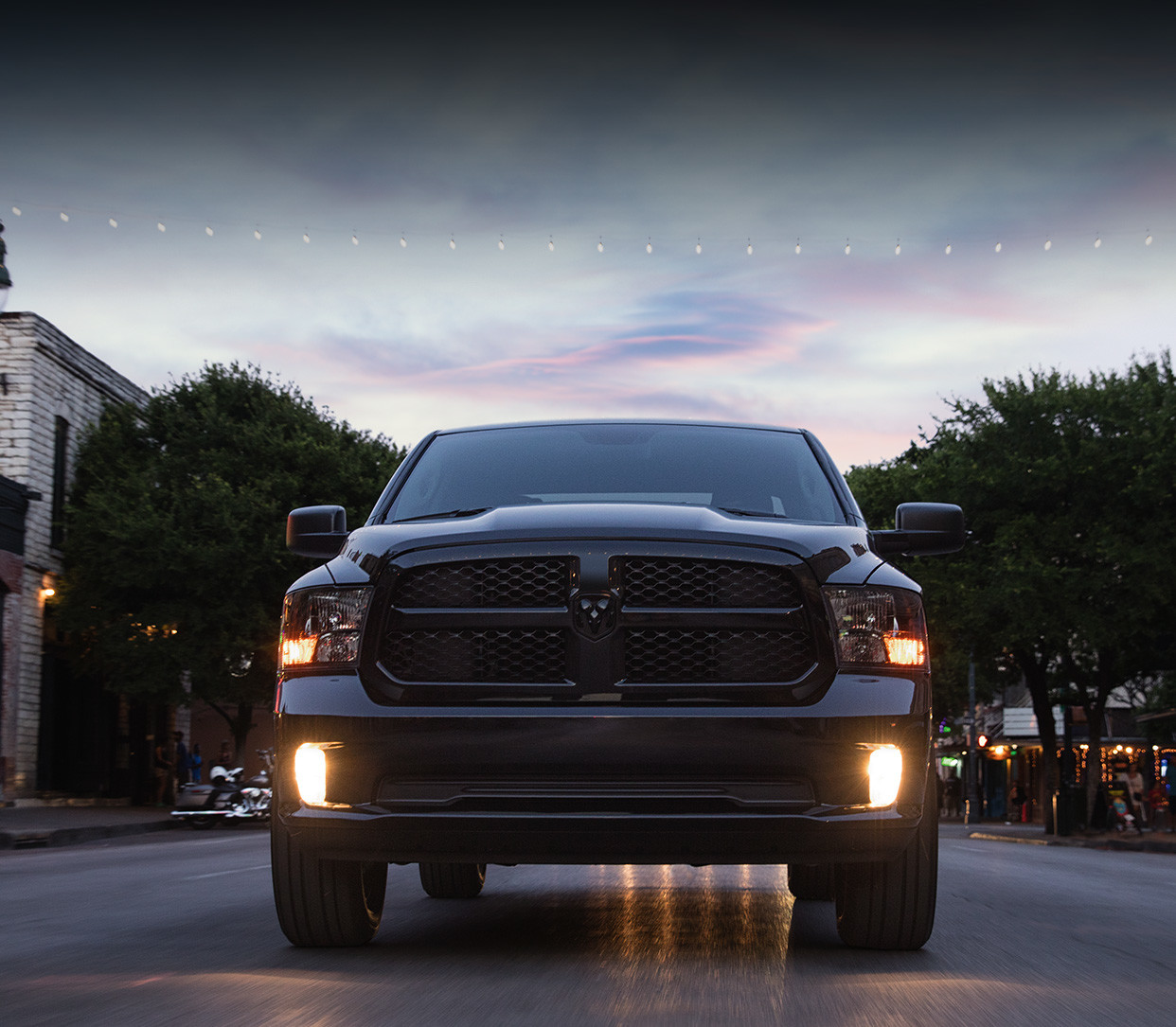 Front view of the black 2020 Ram 1500 Classic driving on a town street at sunset.
