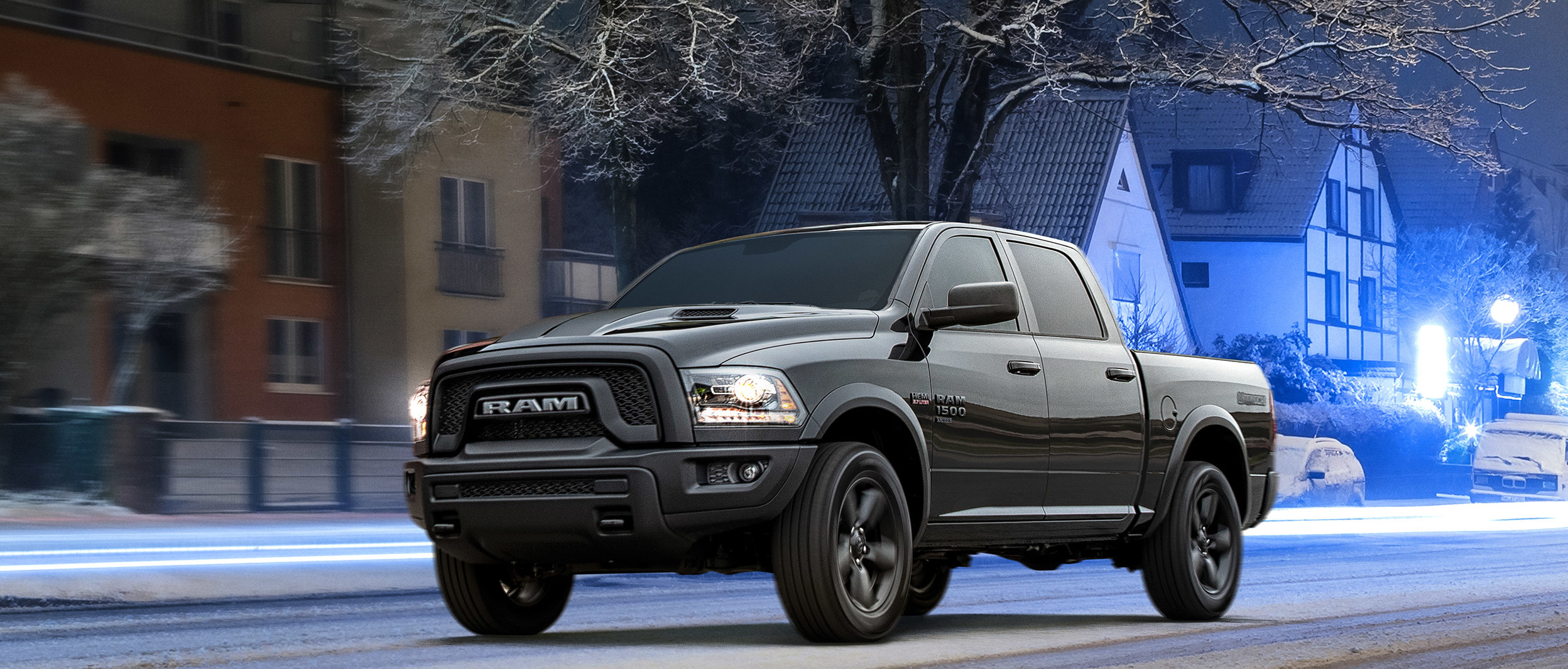 Ram 1500 DS noir roulant sur une route résidentielle calme, un lampadaire étant allumé au-dessus du véhicule.