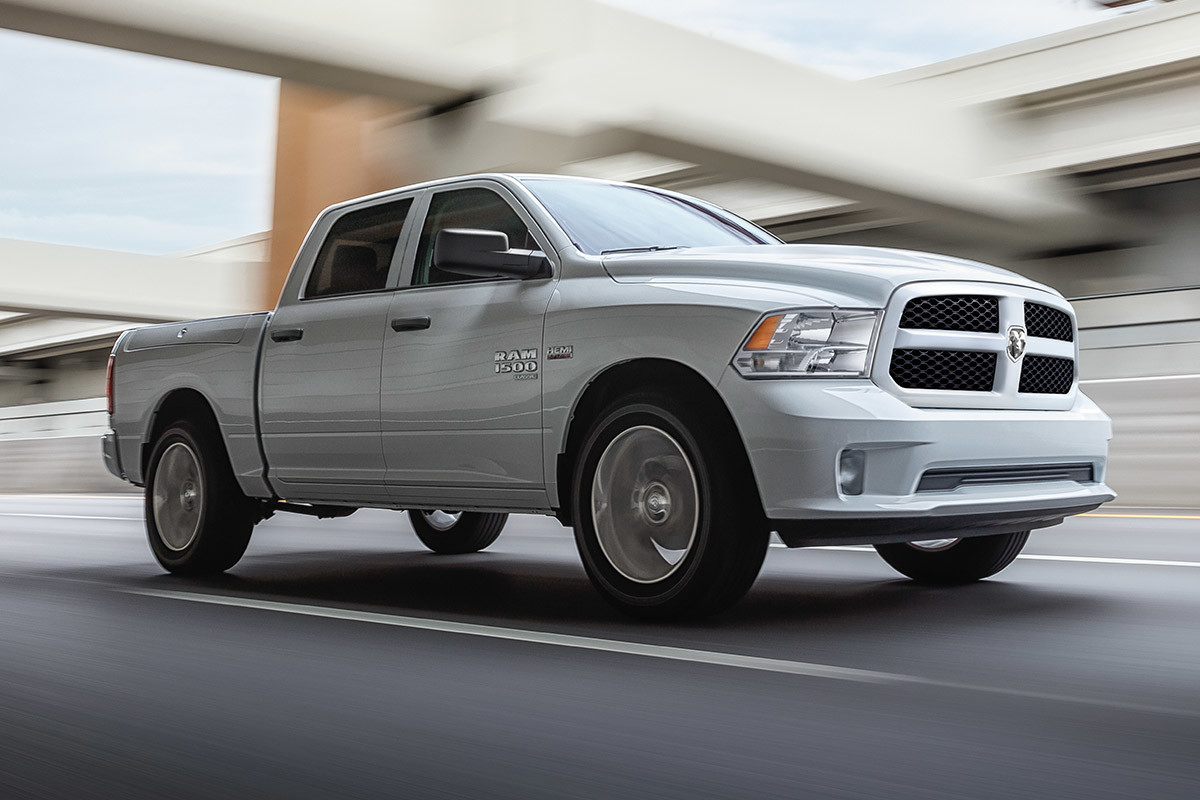 Vue latérale d’un Ram 1500 Classic 2021 blanc éclatant roulant sur une route sous un viaduc.