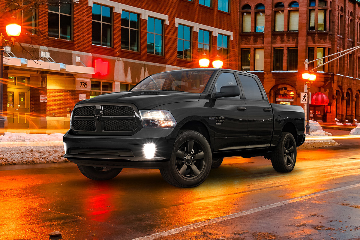 Vue latérale d’un Ram 1500 Classic 2021 couche nacrée cristal noir étincelant garé sur une route urbaine balayée par la pluie la nuit.