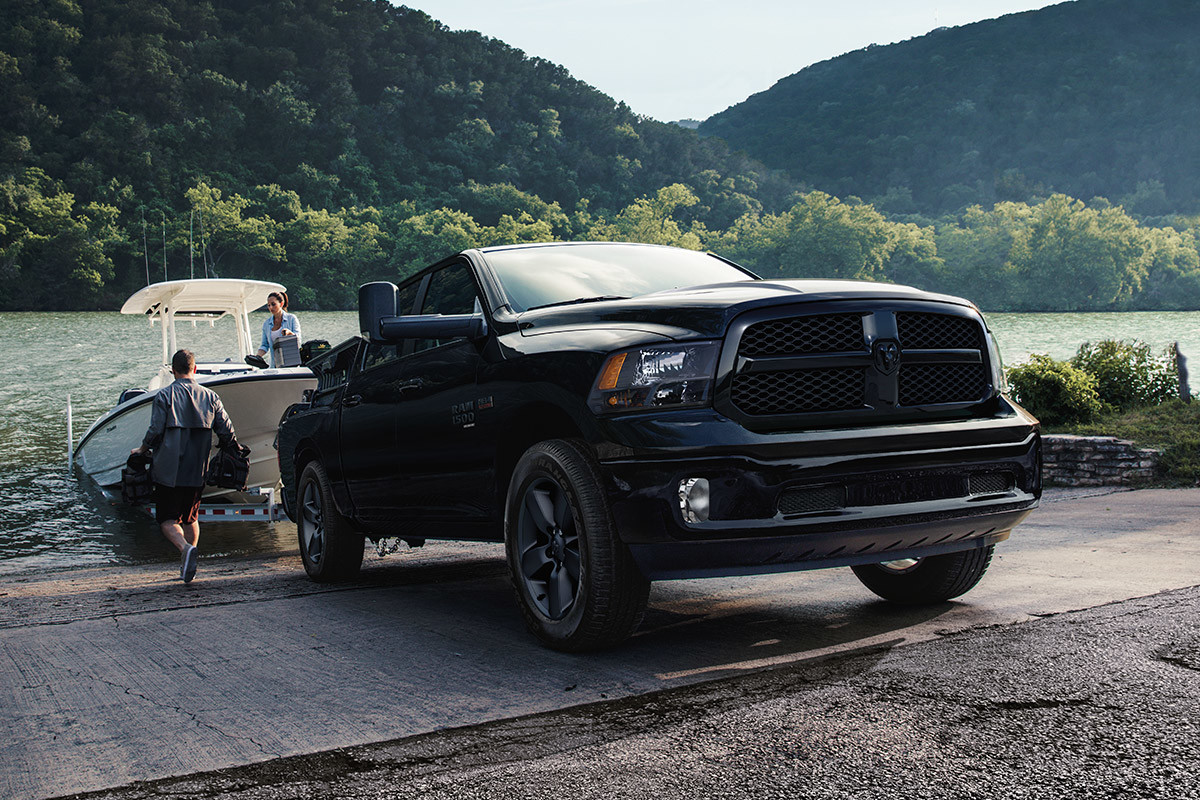 A front view of a man preparing to tow a boat on a trailer from a lake with a Diamond Black Crystal Pearl 2021 Ram 1500 Classic.