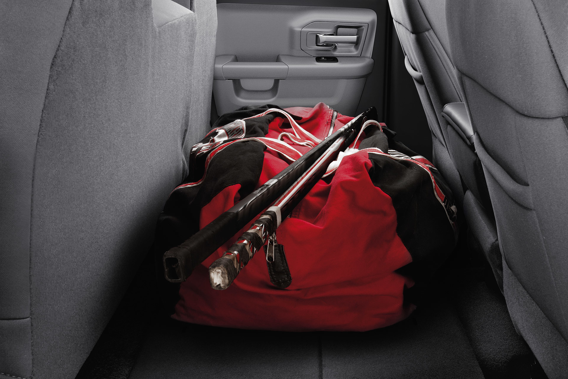 Gros plan d’un sac de hockey rouge et de bâtons de hockey rangés sur la banquette arrière rabattue du Ram 1500 Classic 2021.