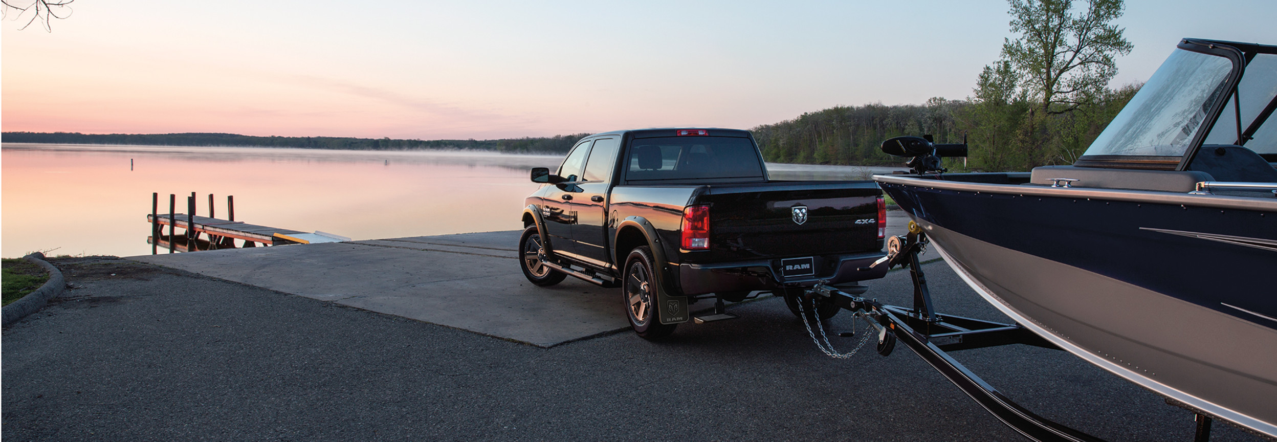 A black 2022 Ram 1500 Classic towing a boat, with trees and a lake in the background.