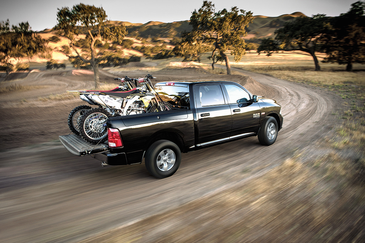 Ram 1500 Classic 2022 noir, chargé de deux motos tout-terrain sur la caisse, roulant sur un chemin de terre.