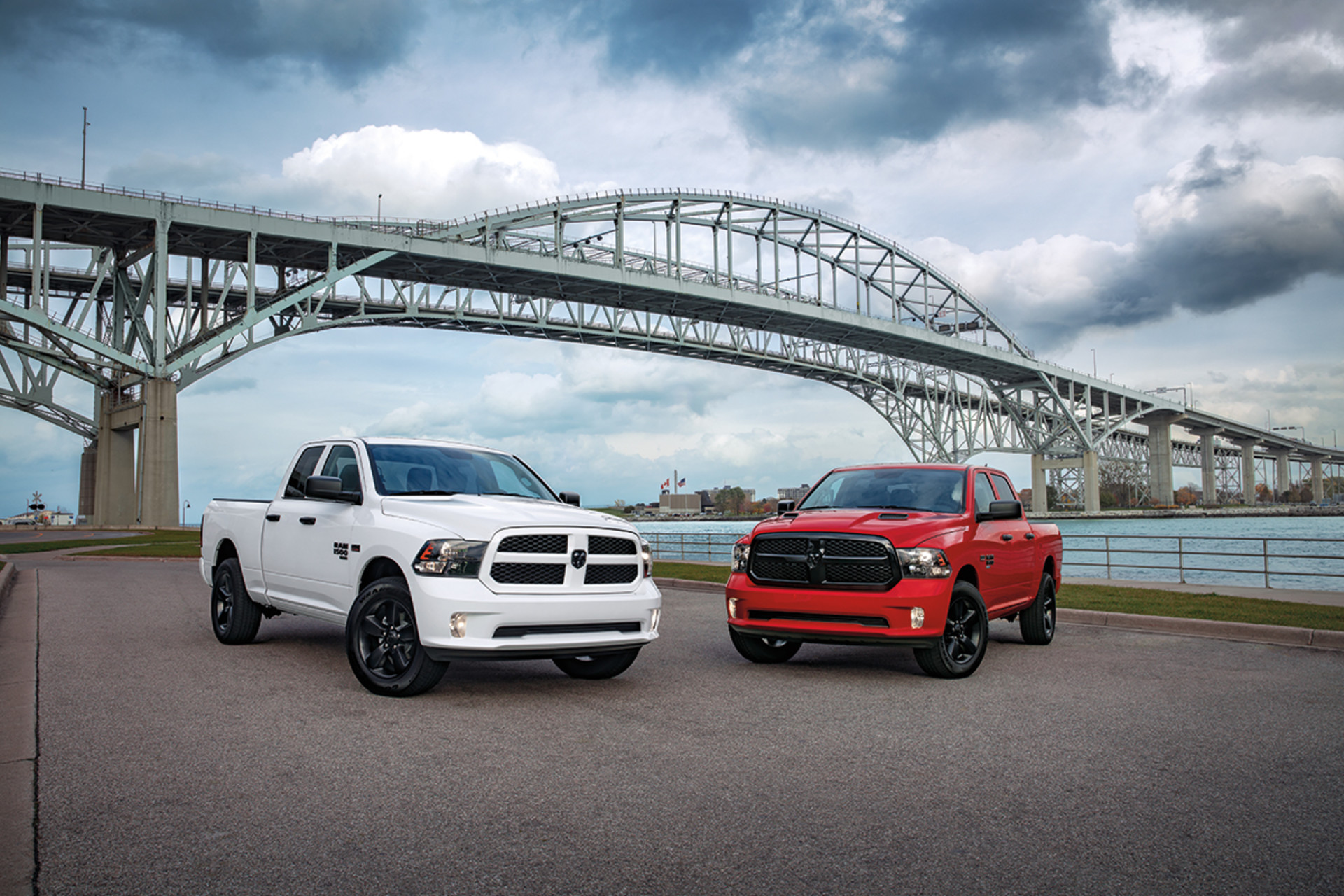 Two 2022 Ram 1500 Classics, one in white, and one in red, parked by a pier with a bridge in the background.