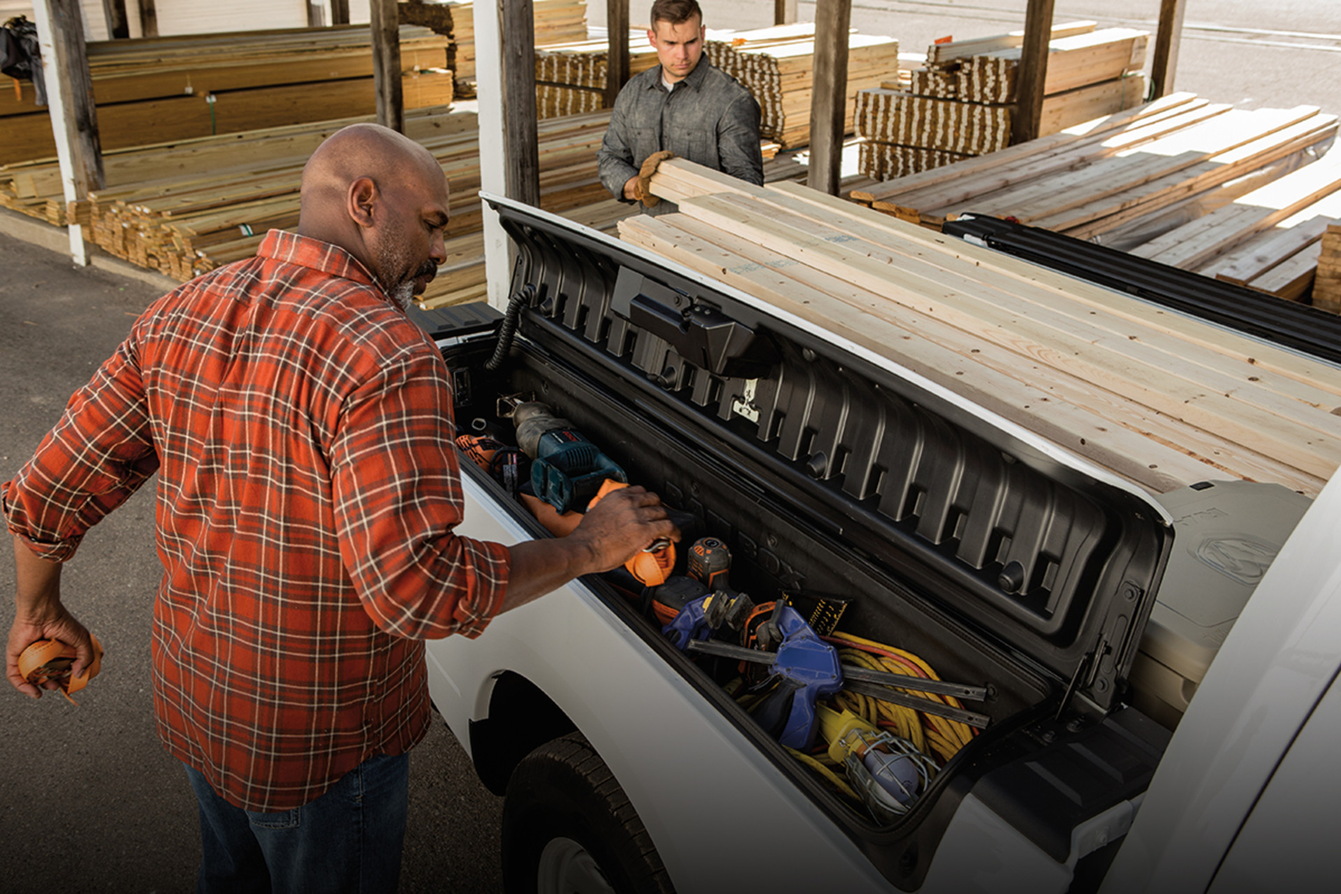 Two people loading the RamBox of a 2022 Ram 1500 Classic with various tools.