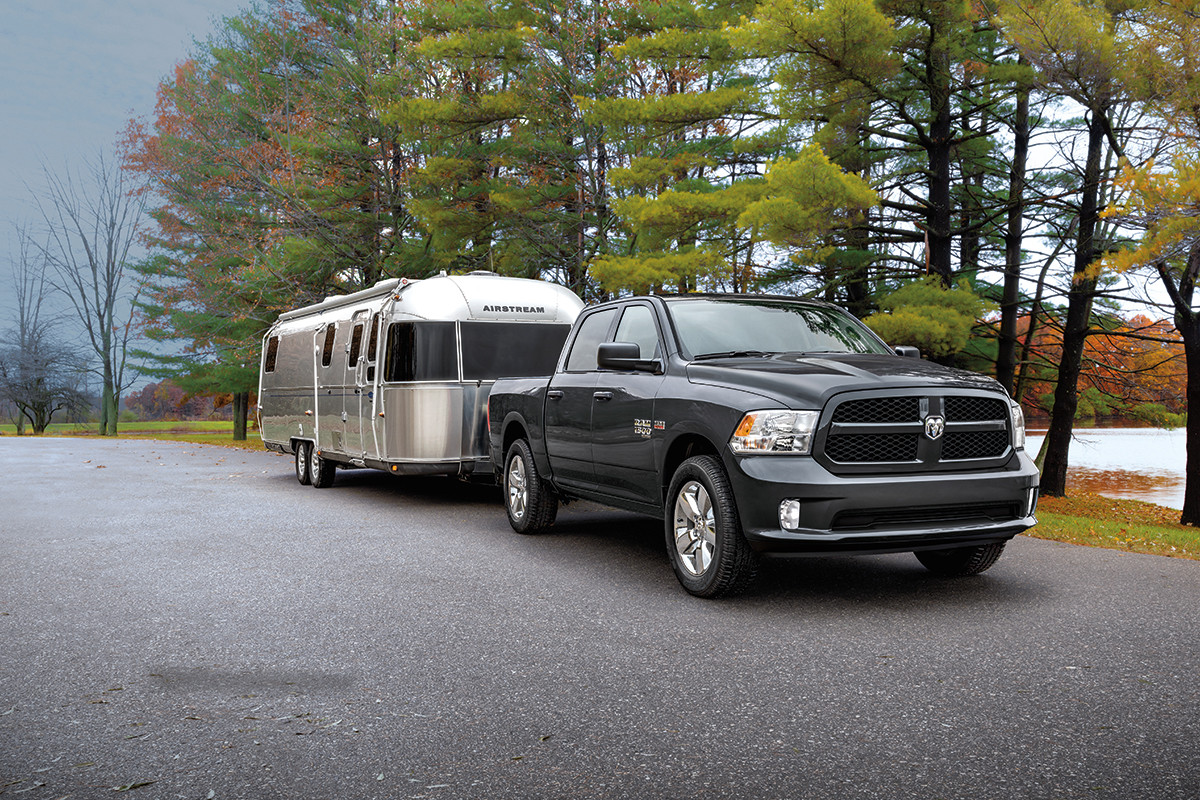 A black 2022 Ram 1500 Classic, towing a travel trailer on a paved road with trees in the background.