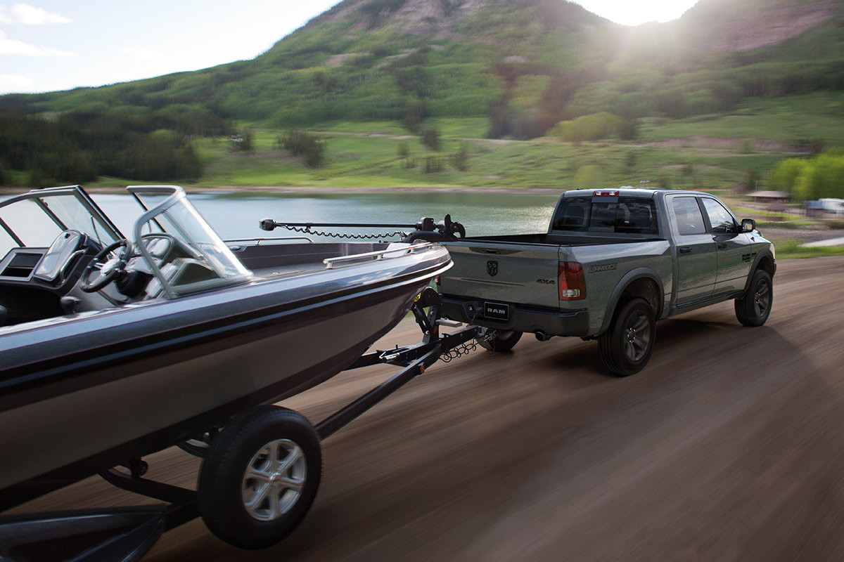 Vue de profil arrière d’un Ram 1500 Classic 2023 gris tirant un bateau noir sur une route pavée.