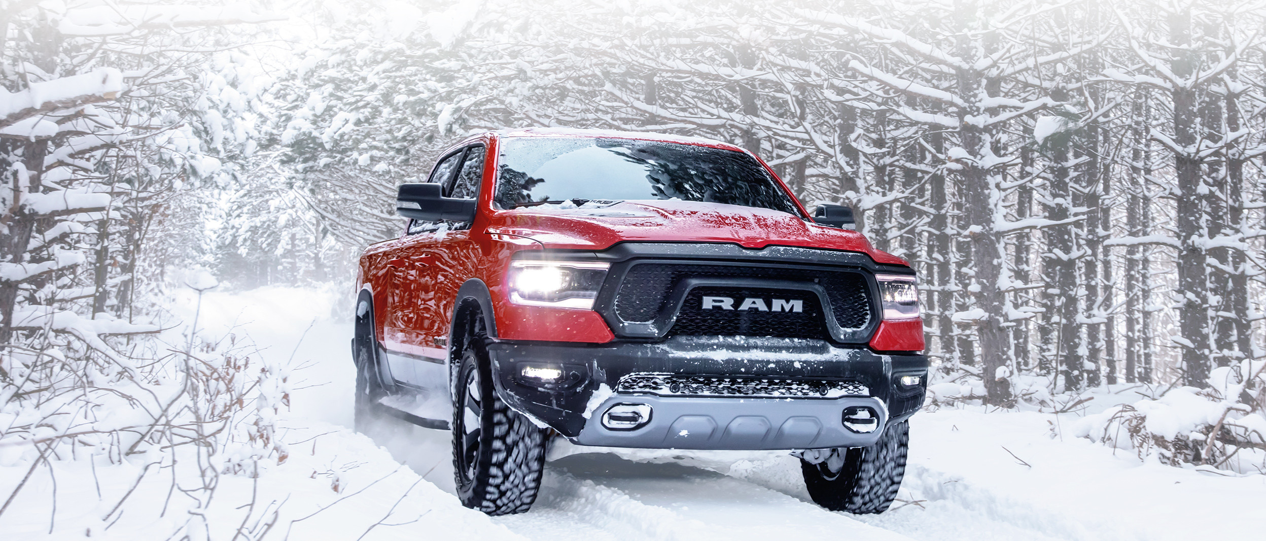 Front view of a 2019 Ram 1500 DT in red driving through a forest on a snow-covered road.