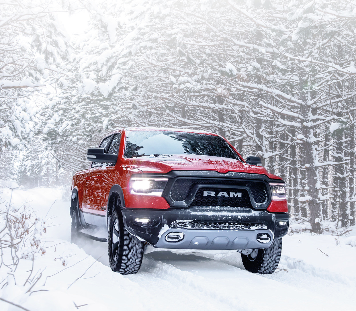 Front view of a 2019 Ram 1500 DT in red driving through a forest on a snow-covered road.