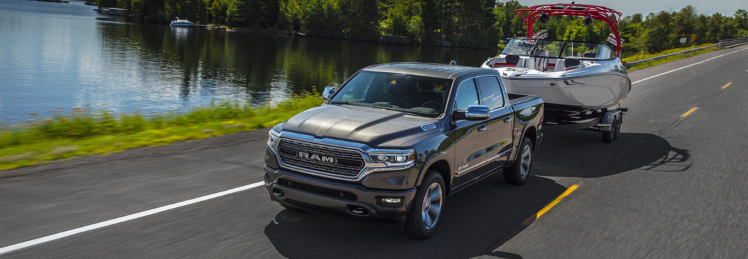 Un RAM 1500 noir remorquant un bateau hydropropulsé sur une route, avec une rivière sur le côté