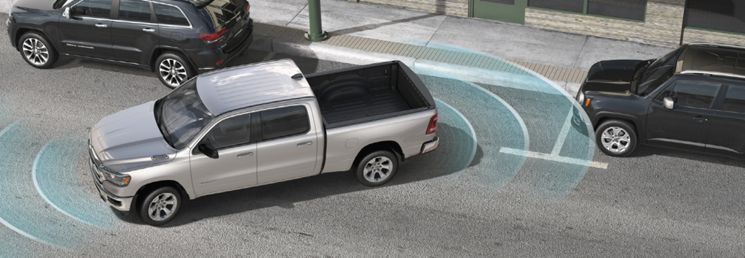 Un RAM 1500 argenté utilisant ses capteurs d’aide au stationnement pour se garer entre deux voitures sur une route