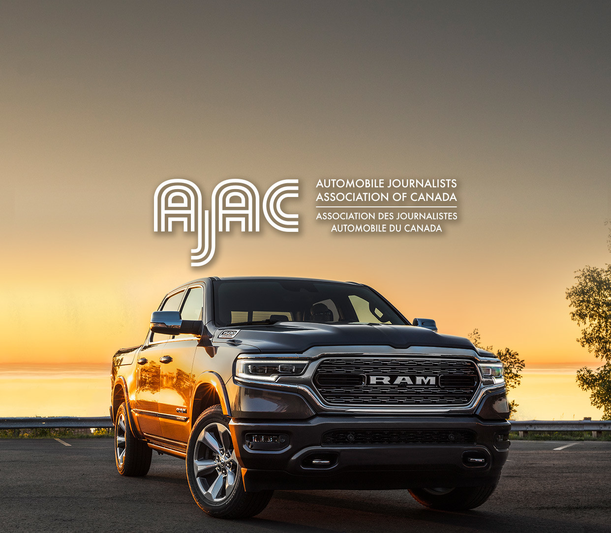 Front view of the 2020 Ram 1500 in black parked in front of the lake at sunset with the AJAC logo on top.