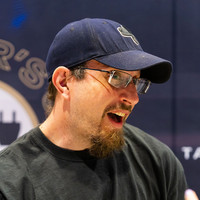An image showing a man in glasses and a blue baseball cap in an interview setting.