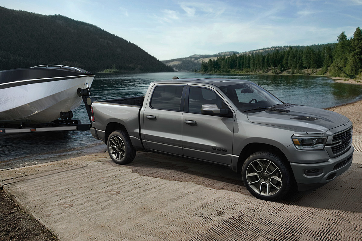 Silver 2021 Ram 1500 pulling a boat out of a lake on a trailer.