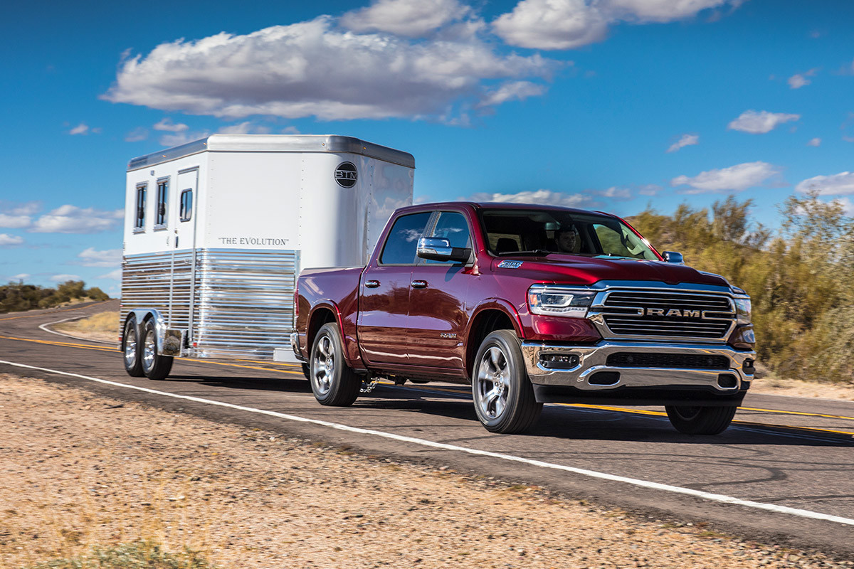 Vue latérale d’un Ram 1500 DT 2021 illustré en couche nacrée rouge tirant une remorque à chevaux sur une route de campagne