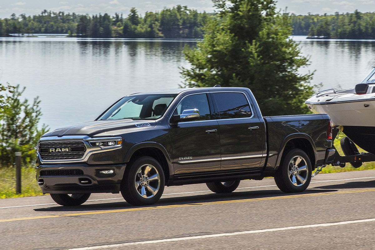 Blue 2022 Ram 1500 towing a boat on a waterfront highway