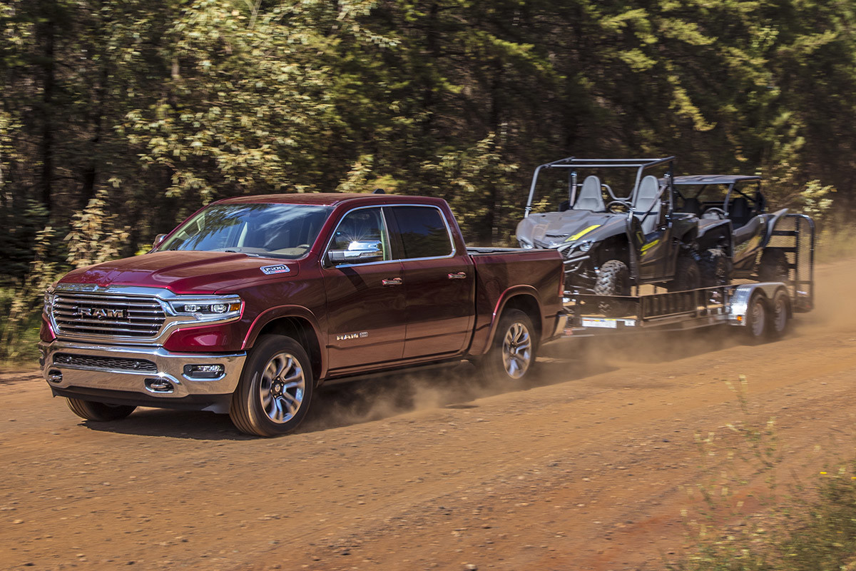 Ram 1500 DT 2022 rouge remorquant deux 4x4 sur un chemin de terre.