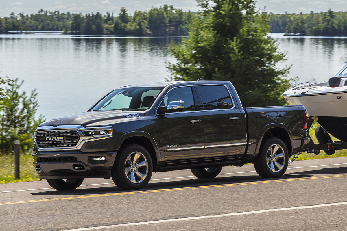 Ram 1500 2022 bleu remorquant un bateau sur une autoroute au bord de l’eau.
