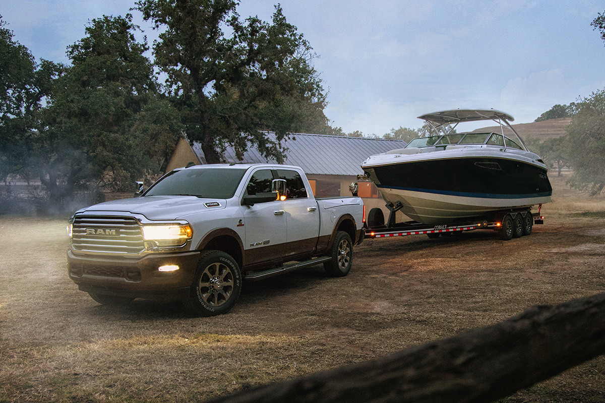Front three quarter view of pearl white the new 2019 Ram 2500 towing a boat trailer parked in a drive way