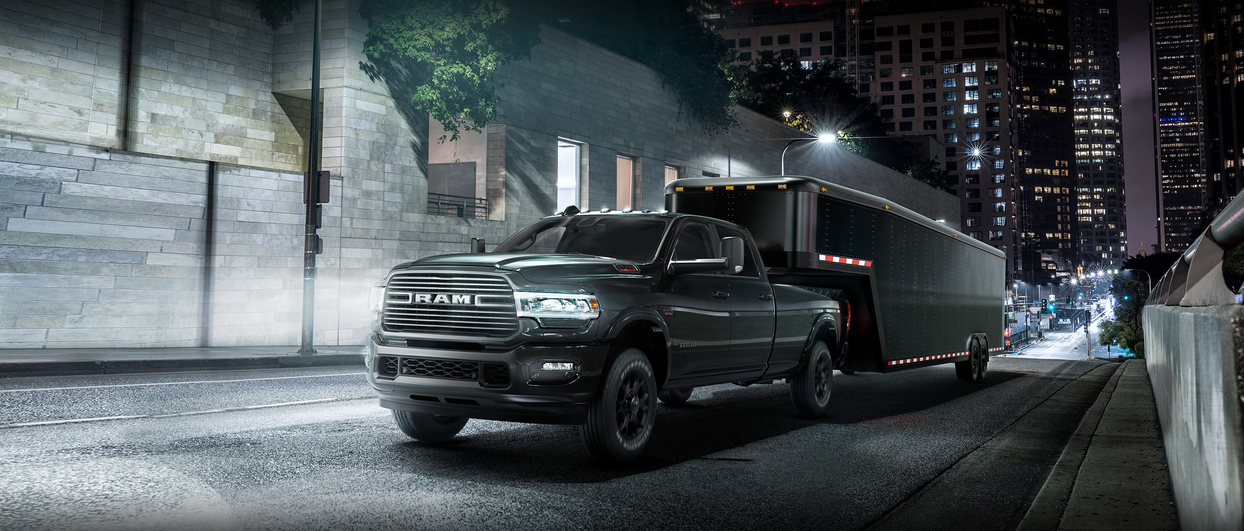 Front three quarter view of the New 2019 Ram 2500 in steel metalic colour towing a trailer on a city street at night