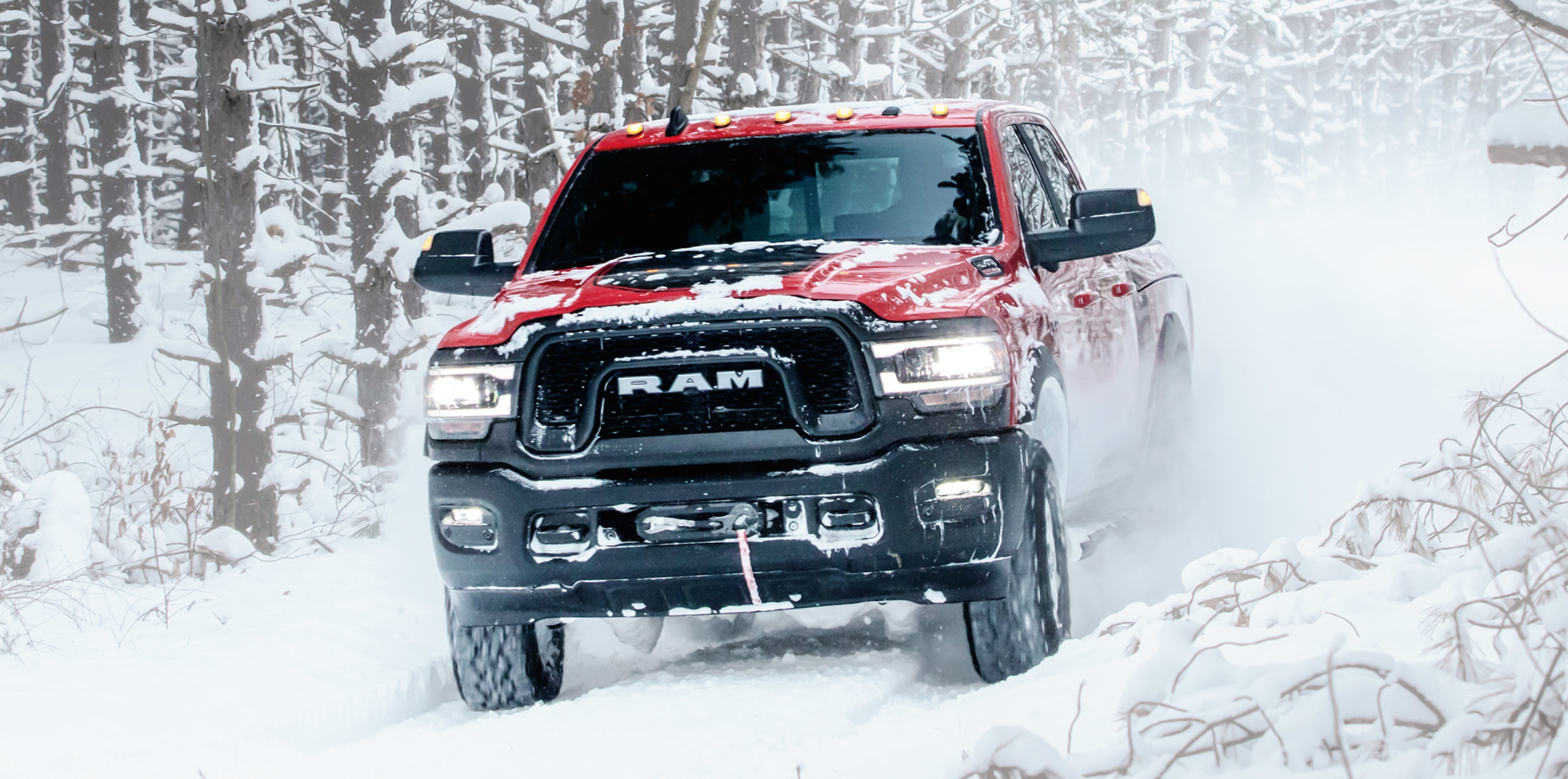 Vue avant d’un Ram 2500 rouge roulant sur une route enneigée avec des arbres en arrière-plan.